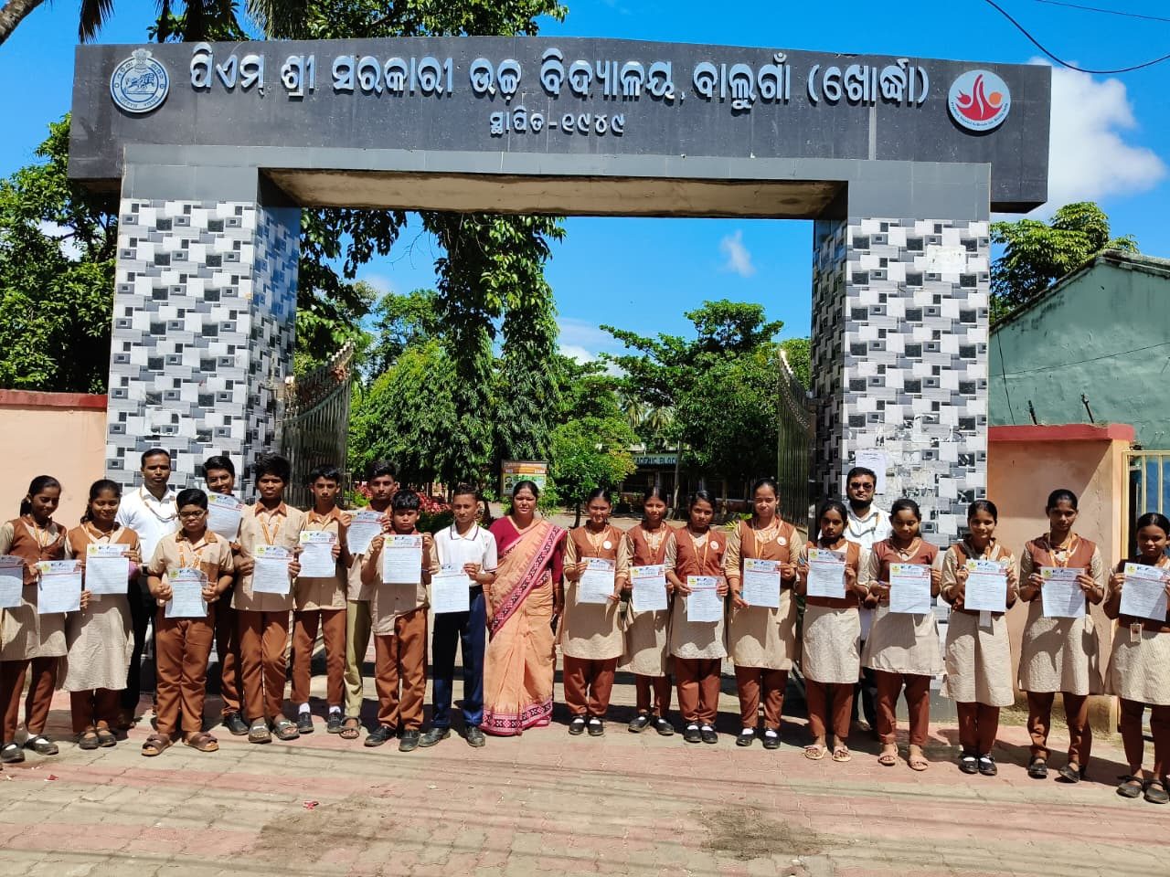 Students with certificates in front of the school gate